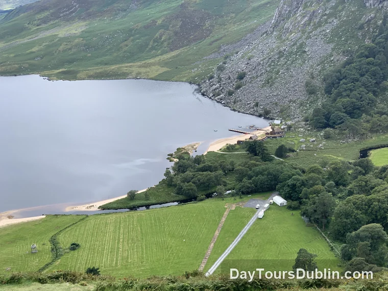 Lough Tay viewed from above, showing the white sandy shore, dark water, shoreline buildings and a small harbor set below steep mountain slopes