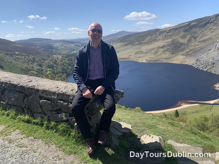 Tour guide Michael Fox seated above Lough Tay with the Wicklow Mountains and the dark lake behind him